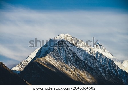 Atmospheric alpine landscape with two rocky pointy mountain peaks with snow in golden sunshine under cirrus clouds. Snow on peaked tops. Awesome mountain scenery with beautiful snow-covered mountains.