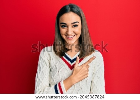 Young brunette girl wearing casual student sweater cheerful with a smile of face pointing with hand and finger up to the side with happy and natural expression on face 