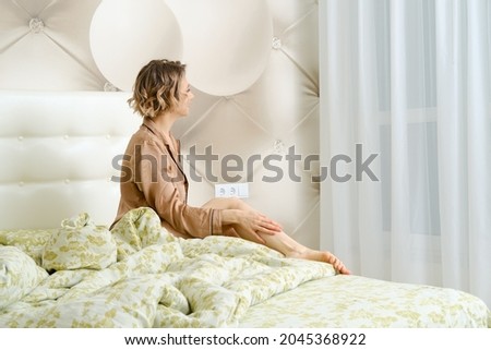Joyful young woman sits on the bed and smiles