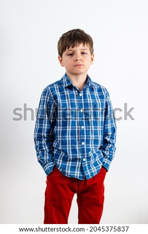 Studio portrait of sad boy keeping hands in pockets of his red pants. Human face expressions, emotions and feelings