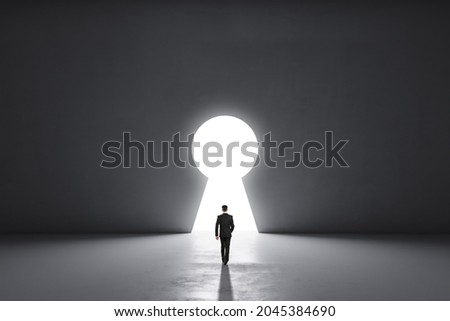 Back view of businessman walking in concrete interior with abstract keyhole window. Key to success and abundance concept. Mock up place Royalty-Free Stock Photo #2045384690