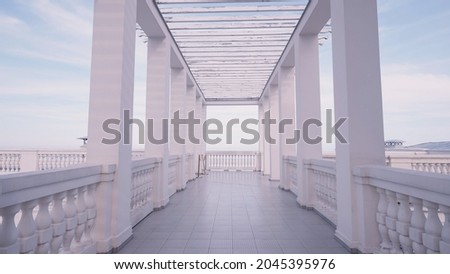 Walking among white marble pillars creating a beautiful corridor on blue sky background. Action. Marble beautiful pier on a summer day.