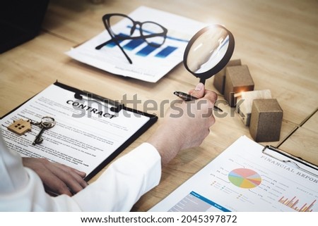 Inspector Concept, a customer is holding a magnifying glass to look at each house model to check the price of a home loan for each model.