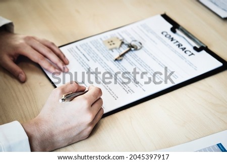 The customer is holding a pen and is reading the housing purchase contract before signing it.