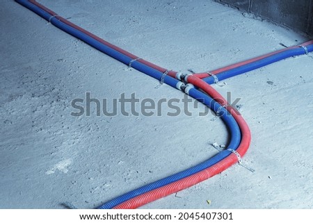 Blue and red plastic corrugated tubes stretched across the floor. Temporary communications of heat and water supply during the repair or construction of a building. Pipe connection point