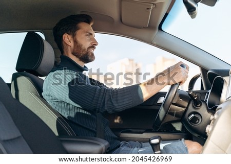 Low angle view of the serious confident man riding at the car and looking at the road during driving. Stock photo Royalty-Free Stock Photo #2045426969