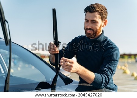 Male auto owner checking windshield wiper at the street. Man is changing windscreen wipers on a car. Automobile repair concept  Royalty-Free Stock Photo #2045427020