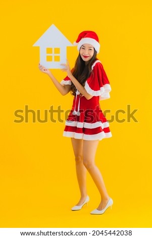 Portrait beautiful young asian woman wear christmas clothes and hat show home house sign with a lot of cash and money on yellow isolated background