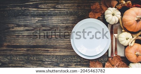 Banner of holiday place setting with plate, napkin, and silverware on a Thanksgiving Day decorated table shot from flat lay or top view position. Pumpkins, antlers and fallen leaves. 