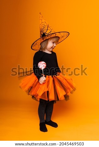 Celebrating Halloween. Little girl dressed as a witch holds a bucket of pumpkins on a yellow background.