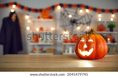 Festive background with smiley beautiful carved Jack-O-lantern pumpkin with burning candle inside placed on wooden table in festively decorated living room. Traditional Halloween celebration concept