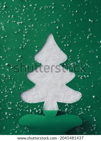 Green card with cutout silhouette of a traditional Christmas Tree over winter snow in a creative template for the Holiday Season with