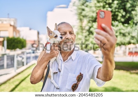 Senior man smihugging chihuahua making selfie by the smartphone at park