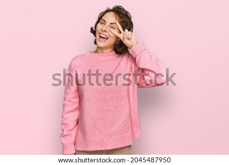 Young hispanic woman wearing casual clothes doing peace symbol with fingers over face, smiling cheerful showing victory 