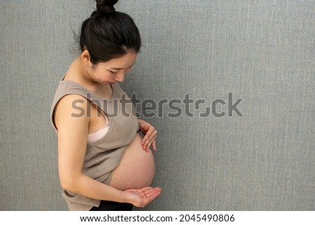 A young pregnant Asian woman applys body lotion to her stomach not to make pregnancy stretch mark
