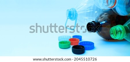 Plastic bottles and lids on a light background. Banner, copy space. The concept of separate sorting of plastic, rejection of plastic, production of plastic bottles.