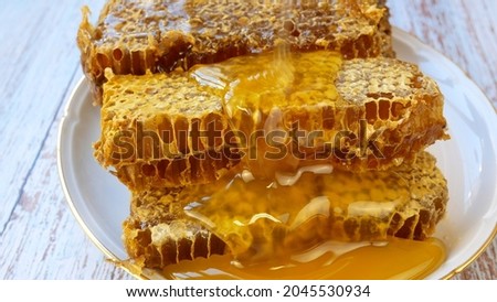 Liquid golden sweet honey is poured on top of the honeycomb. Honey flows down the waxy combs. Harvesting honey in the apiary Royalty-Free Stock Photo #2045530934