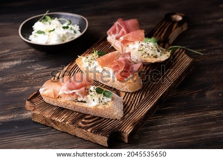 Toast with prosciutto ricotta and microgreens, ham crostini on a dark wooden background, rustic style. Royalty-Free Stock Photo #2045535650