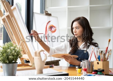 Pretty Asian woman painter painting on canvas at art studio.