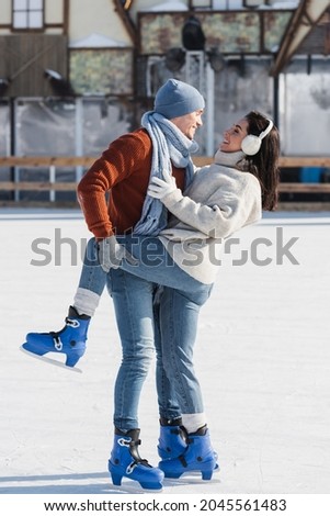 full length of cheerful man lifting leg of happy girlfriend on ice rink