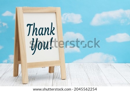 Thank you sign standing whiteboard on weathered wood with clear sky