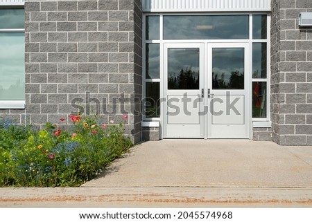 Double commercial exterior doors of a business. The glass is on top, trim is stainless steel metal. The doors have metal handles. There are large grey brick walls on both sides of the doors.  Royalty-Free Stock Photo #2045574968