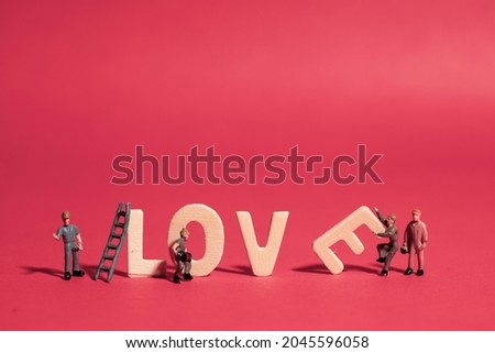A small worker doll is building the lettering for love on a red background.