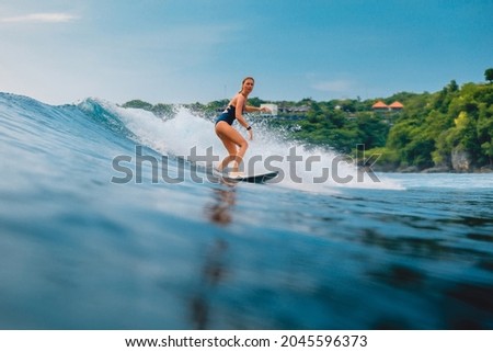 Surf girl at surfboard on blue wave in Bali, Impossibles beach. Sporty woman in ocean during surfing.