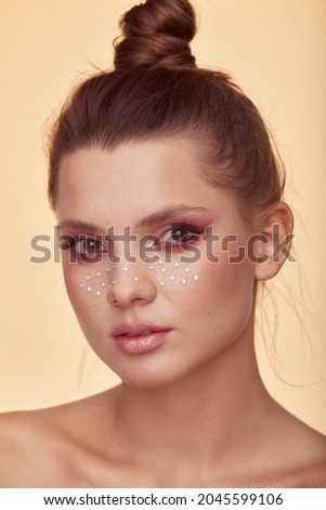 Fashion creative make up. Beautiful portrait of young woman with clean fresh skin and bright make up with rhinestones freckles on her face posing on a yellow background Royalty-Free Stock Photo #2045599106