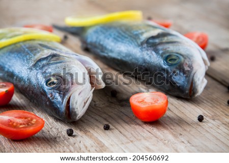 Two raw seabass fish with cherry tomatoes on a rustic wooden background