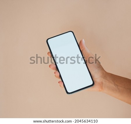 An Anonymous Woman Holding Mobile Phone with Empty Screen on Orange Background.
 
Close up photo of female hand showing smartphone with blank screen isolated over a peach background.