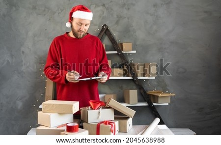Caucasian bearded man wearing santa claus hat and red sweater business owner working at home. christmas gift shopping concept. marks boxes for delivery.Place for text