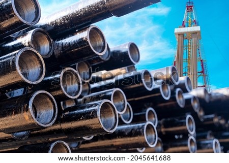 In the foreground pipes for drilling oil and gas wells. In the background, a blurred image of the rig out of focus. Blue sky with clouds. Royalty-Free Stock Photo #2045641688