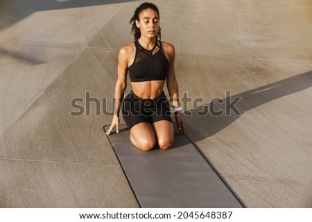 Black sportswoman doing exercise while working out on fitness mat on parking outdoors
