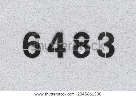 Black Number 6483 on the white wall. Spray paint. Number six thousand four hundred and eighty three.