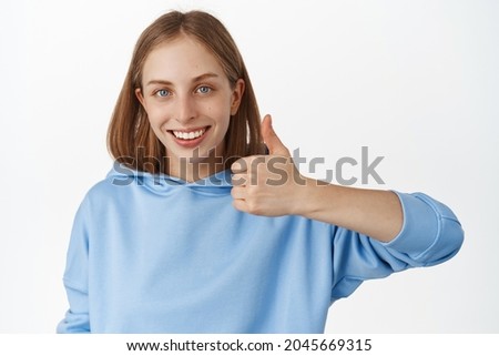 Very good, yes. Smiling young blond woman showing thumb up and look confident, recommend great place, like and approve smth, praise you, standing against white background
