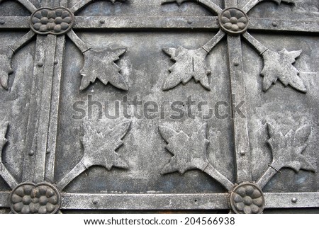 Grey metallic door of an old church decorated by floral ornament.