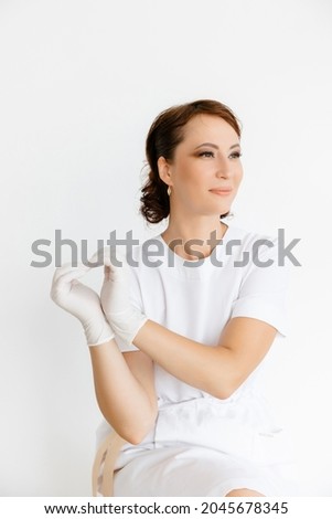 a girl in a white coat smiles and shows a heart symbol with her hands in white rubber gloves. the room is on a white background. The concept of cosmetology and medical services.