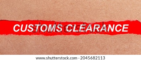 A strip of red paper under the torn brown paper. White lettering on red paper CUSTOMS CLEARANCE. View from above