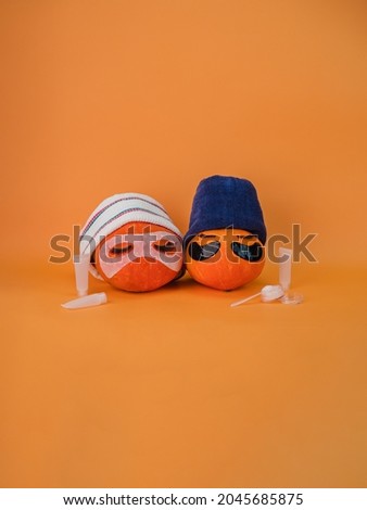 Two pumpkin with eye patches, facial mask and towel on orange background, copy space. Skin care accessories, Halloween.