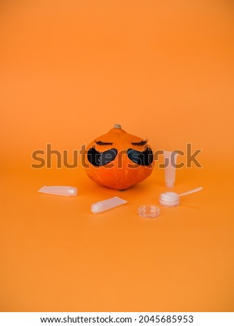 Pumpkin with eye patches on orange background, copy space. Skin care accessories, Halloween.