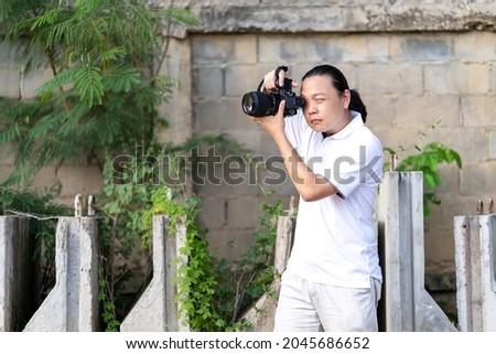 Professional Asian Chinese - Thai Camera man posture and focus in viewfinder and LED screen on mirrorless camera medium format in construction concrete area.