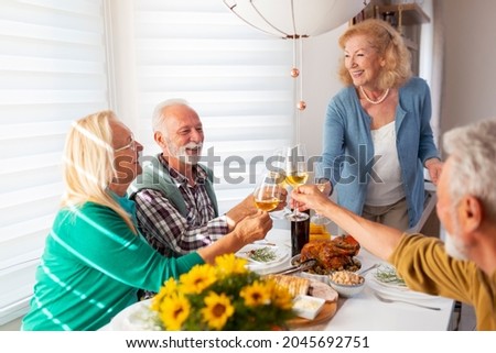 Group of senior people having fun while celebrating Thanksgiving together at home over traditional dinner, making a toast raising glasses of wine