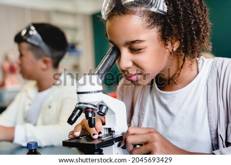 African-american schoolgirl pupil student using working with microscope at biology chemistry lesson class at school lab. Science lesson concept Royalty-Free Stock Photo #2045693429