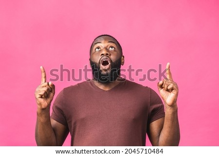 Portrait of happy young african american black man with in casual smiling, pointing up with finger, looking in camera with excited face expression isolated over pink background.