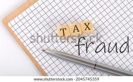 TAX FRAUD text concept written on wooden cubes blocks and notebook