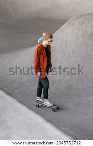a young and beautiful woman skater. a woman in an orange jacket rides a skateboard on a skate pad. extreme sports. a confident European woman is learning to ride a board on a skate pad. modern