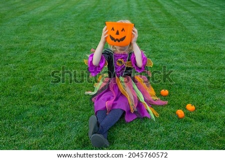 Funny happy little girl in halloween costume is sitting on grass.
