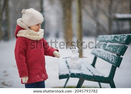 Adorable toddler girl building a snowman on a day with heavy snowfall. Happy child playing with snow. Winter activities for kids