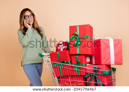 Portrait of beautiful trendy cheerful woman carrying giftboxes talking on phone isolated over beige pastel color background